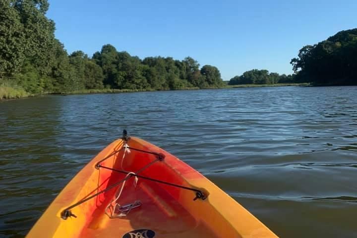 Orange kayak on calm river with tree-lined banks under clear blue sky.