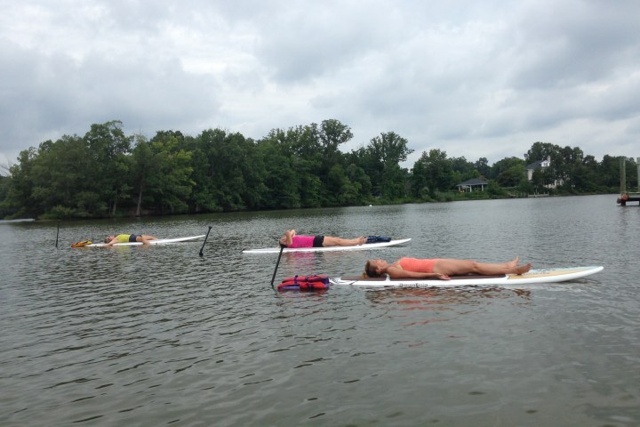 Three people relaxing on paddleboards on a lake under a cloudy sky.