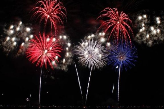 Red, white, and blue fireworks exploding over water at night.