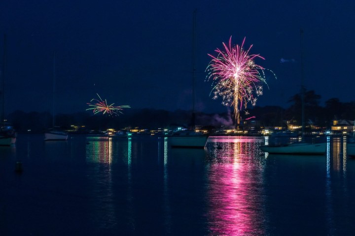 Colorful fireworks over a calm lake with reflected lights and boats visible at night.